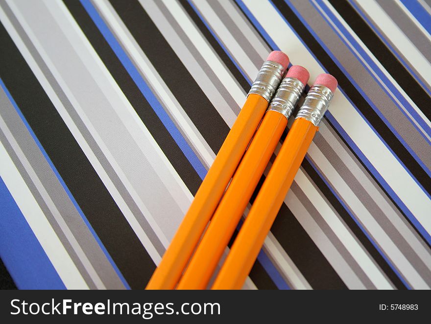 Three pencils laying on a striped notebook which makes for a cool background.