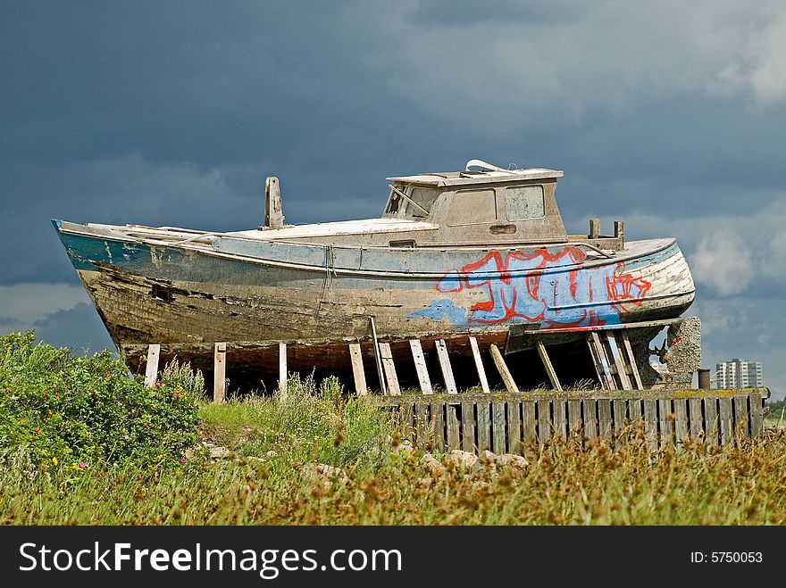 Vintage and leaky boat on land under dark and heavy skies