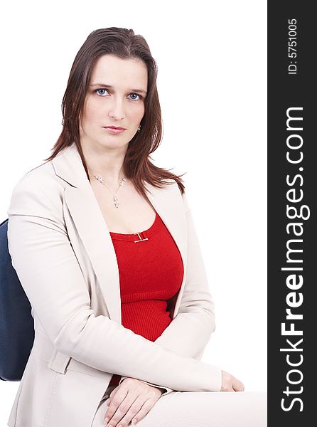 Beautiful brunette businesswoman wearing a beige jacket and a red top, sitting on the office chair. Isolated on white background with copy space