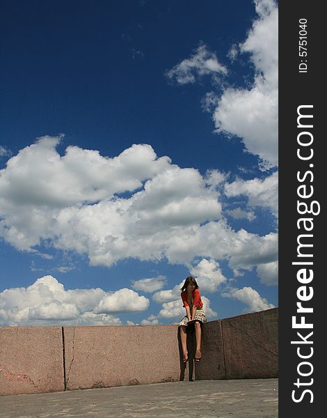 The young girl sits on a border of a roof on a background of the is bright-dark blue sky with snow-white clouds. The young girl sits on a border of a roof on a background of the is bright-dark blue sky with snow-white clouds