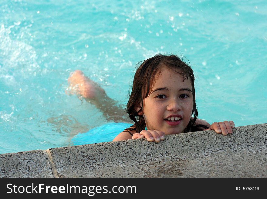 A 6-year-old girl holds onto the edge of a swimming pool. She has big brown eyes and brown hair and is of Asian and Caucasian background, multi-racial. A 6-year-old girl holds onto the edge of a swimming pool. She has big brown eyes and brown hair and is of Asian and Caucasian background, multi-racial.