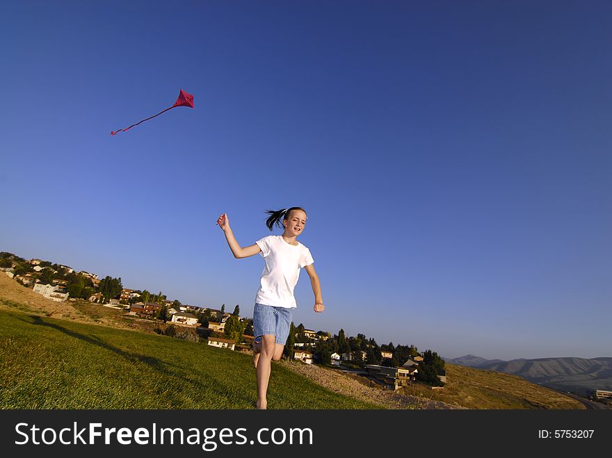 Girl running and flying a kite in a park with blue sky