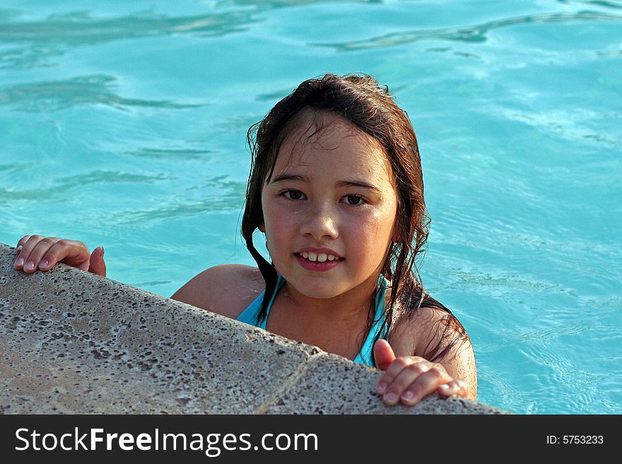 A smiling 6-year-old girl holds onto the edge of a swimming pool. She has big brown eyes and brown hair and is of Asian and Caucasian background, multi-racial. A smiling 6-year-old girl holds onto the edge of a swimming pool. She has big brown eyes and brown hair and is of Asian and Caucasian background, multi-racial.