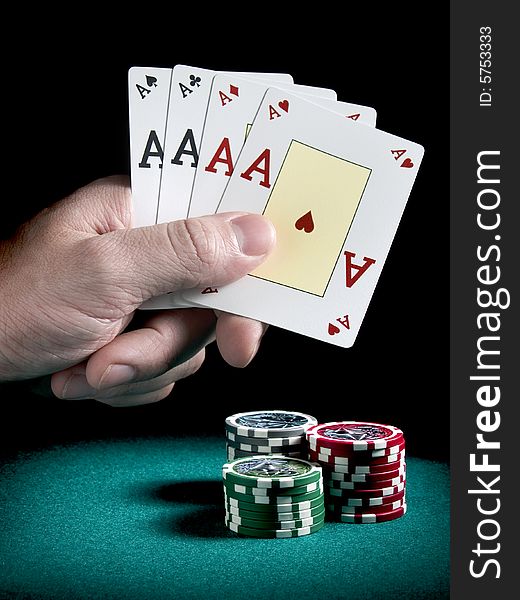 A man's hand holding four aces over three piles of different colors chips on a green felt.