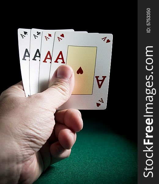 A man's hand holding four aces over a green felt.
