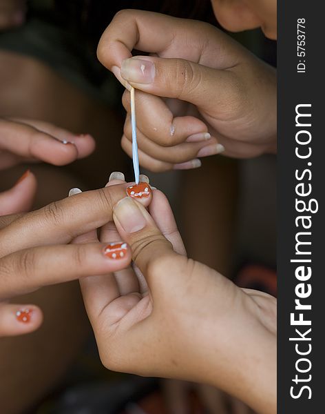 Hand of a woman with long nails, painting the nails of another woman red with black and blue spots. Shallow depth of field. Hand of a woman with long nails, painting the nails of another woman red with black and blue spots. Shallow depth of field.