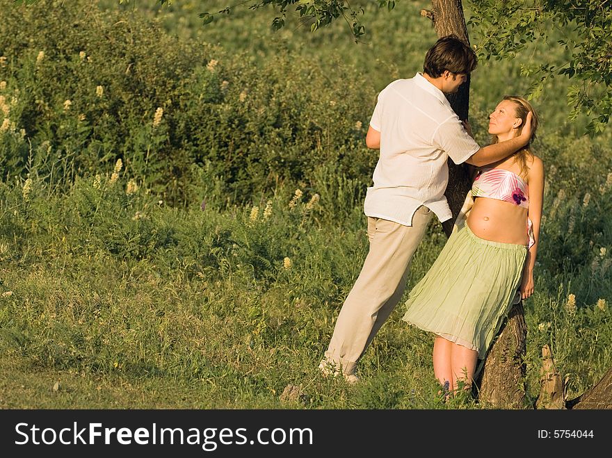 Young happy couple outdoors at a sunset, woman is pregnant