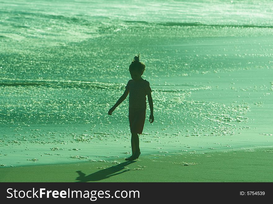 Silhouette of Todler girl walking in water on beach in greenish sunset. Silhouette of Todler girl walking in water on beach in greenish sunset