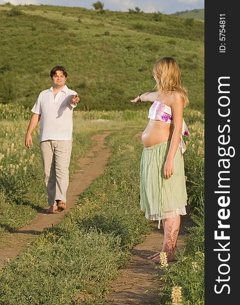 Young married couple on the walk, woman is pregnant and gives her hand to her husband. Young married couple on the walk, woman is pregnant and gives her hand to her husband