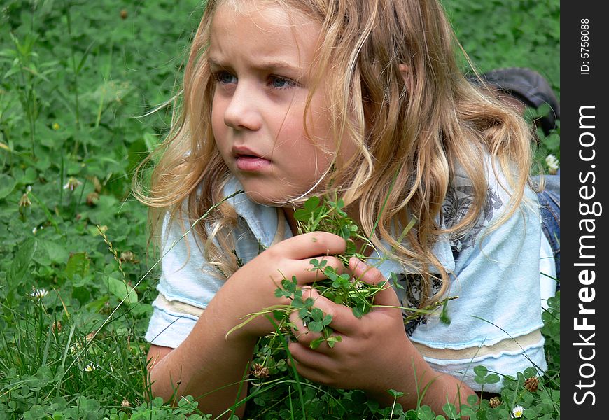 Boy with long blond hair is lying in the grass and holding trifolium. Boy with long blond hair is lying in the grass and holding trifolium