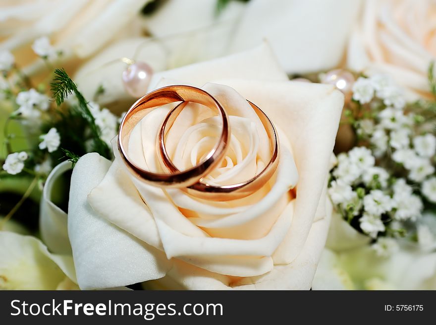 Two rings lie on roses bud on wedding bouquet background. macro