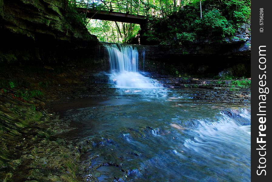 This is a small water fall with a bridge overhead.