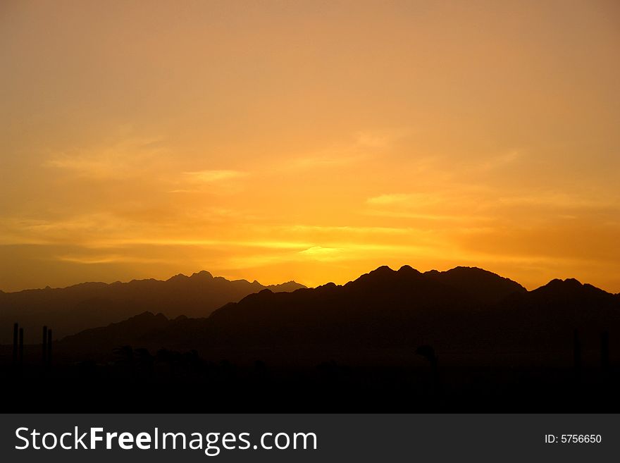The photo of a beautiful sunset in beige, orange and yellow colours in high mountains surrounded by the palms. The photo of a beautiful sunset in beige, orange and yellow colours in high mountains surrounded by the palms