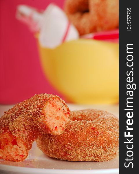 Two freshly made strawberry doughnuts with a bowl of doughnuts in the background. Two freshly made strawberry doughnuts with a bowl of doughnuts in the background