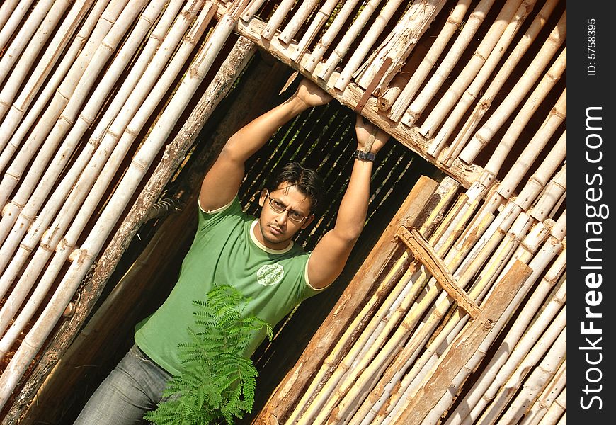 A handsome dude posing, standing in front of a bamboo house