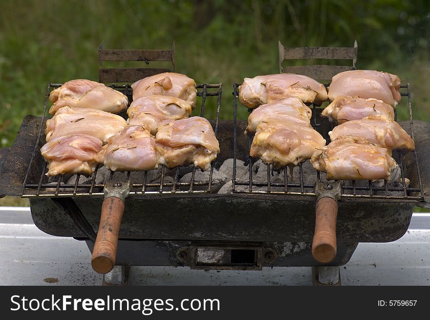 Chicken pieces being grilled on charcoals of hibachi grill.