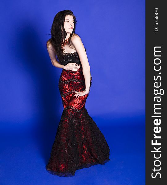 Beautiful young woman wearing a red evening gown in front of a blue background