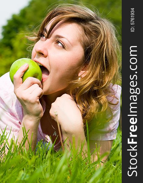 Pretty woman eating green apple on the summer glade