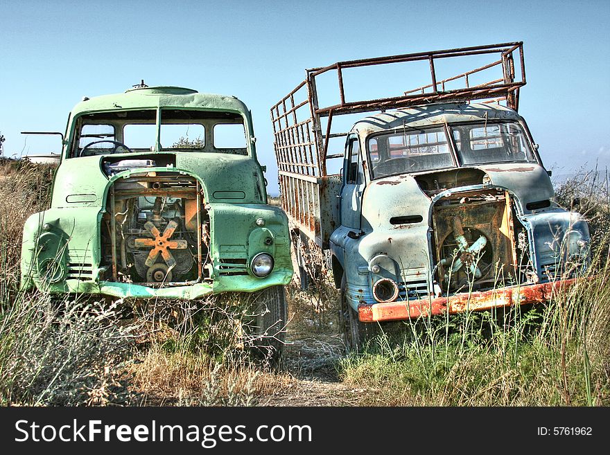 Two abandoned trucks rusting away at the edge of a field