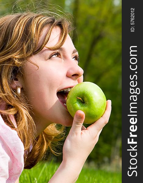 Pretty woman eating green apple on the summer glade