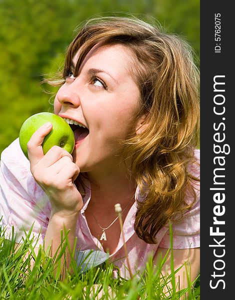 Pretty woman eating green apple on the summer glade