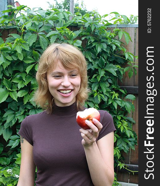 The young smiling girl with red apple on a background of wild grapes. The young smiling girl with red apple on a background of wild grapes.
