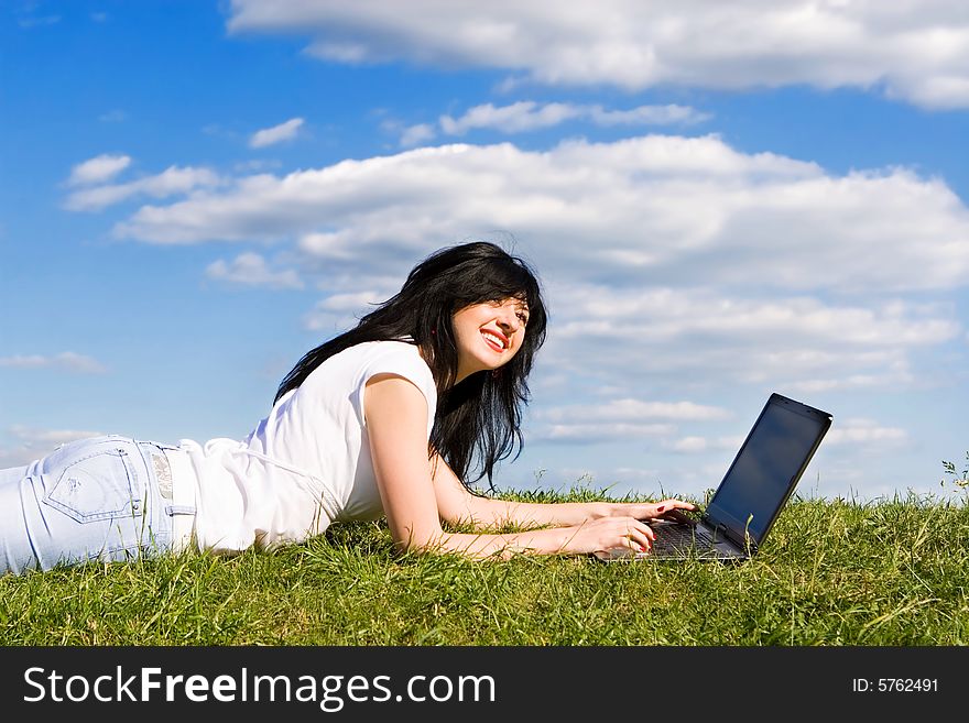 Pretty woman with laptop on the green grass