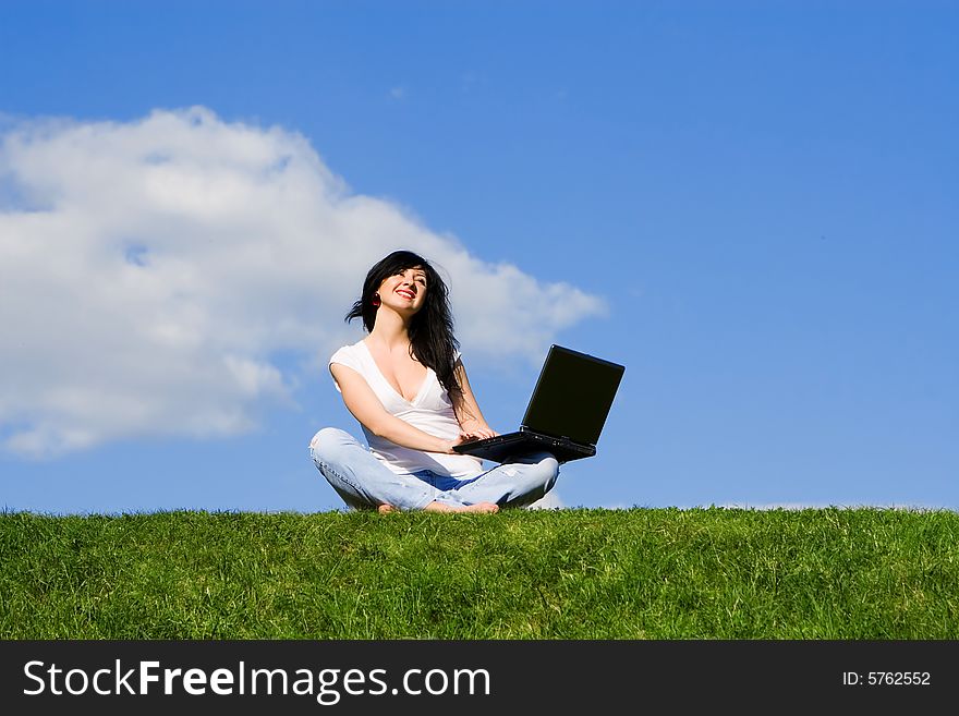 Pretty woman with laptop on the green grass