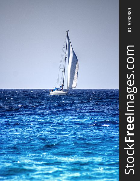 Small white sailing yacht on a calm sea with its main sail up