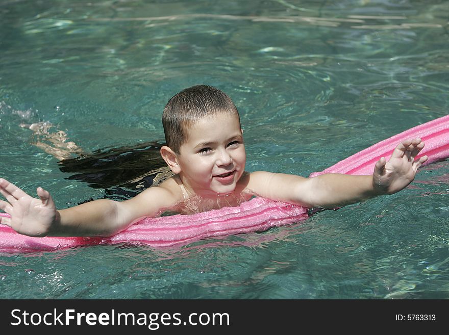 Smiling young boy in crystal clear swimming pool with pink pool toy. Smiling young boy in crystal clear swimming pool with pink pool toy.