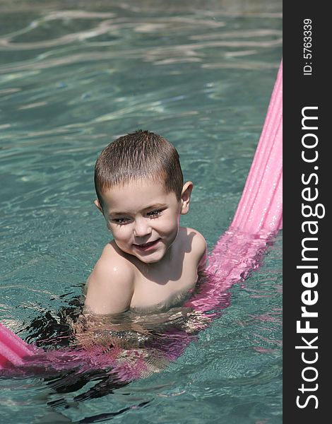 Smiling young boy in crystal clear swimming pool with pink pool toy. . Smiling young boy in crystal clear swimming pool with pink pool toy.