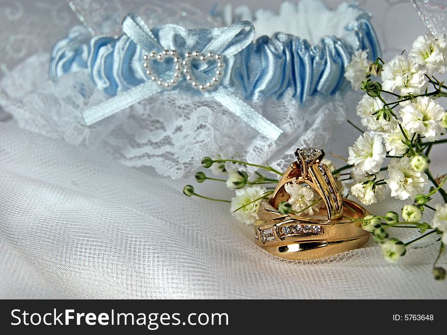 Pair of gold wedding rings and garter on white tulle. Pair of gold wedding rings and garter on white tulle.