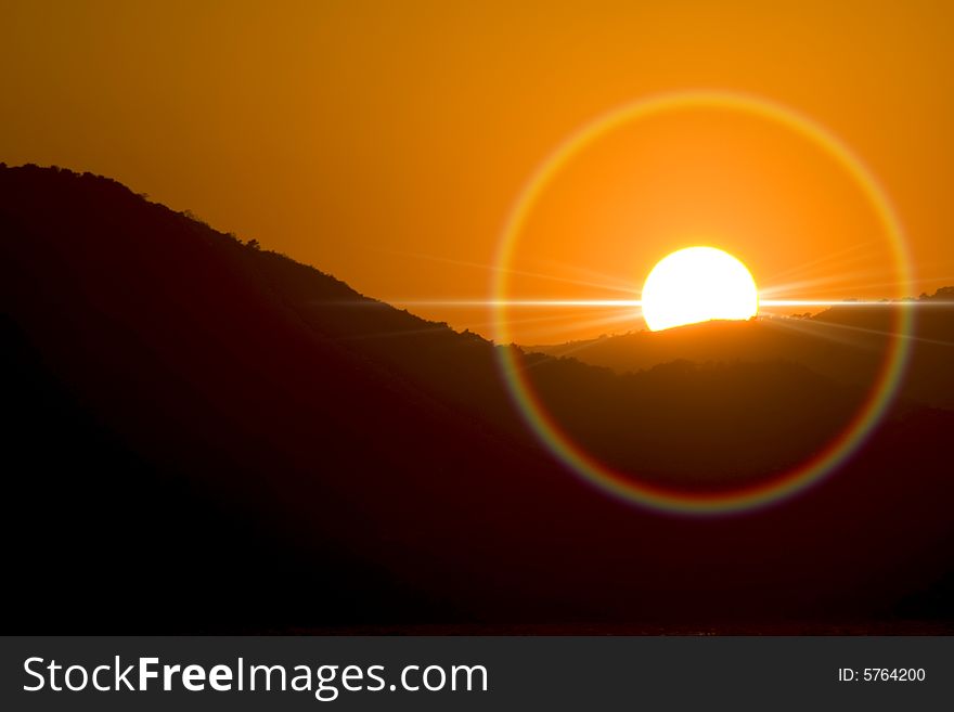 Sunset with halo and sun ray behind mountains