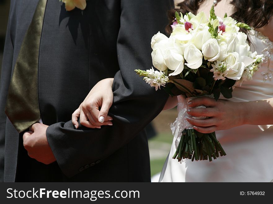 A bride holding a bouquet of white roses with one hand and holding the arm of the bridegroom with the other, during a weddiing ceremony. A bride holding a bouquet of white roses with one hand and holding the arm of the bridegroom with the other, during a weddiing ceremony