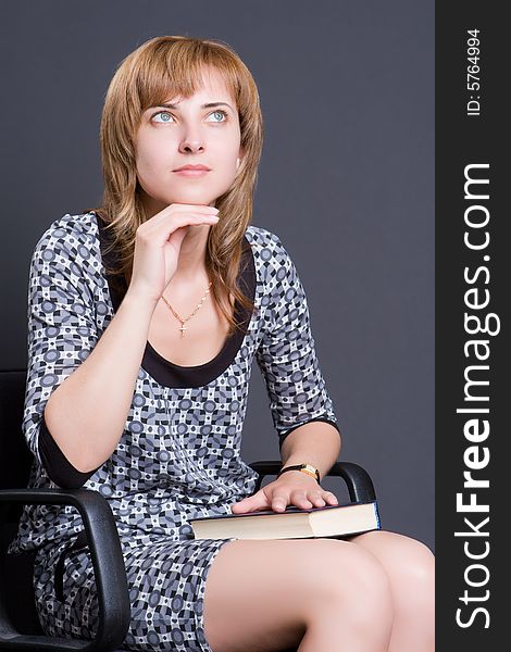 Thoughtful girl sits on an armchair with the book in a lap