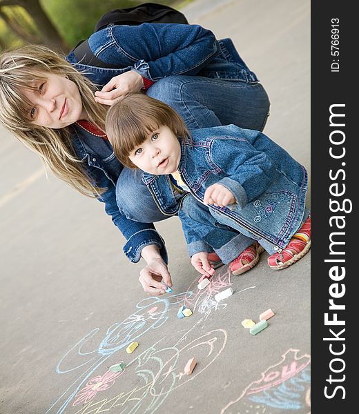 A cute little girl drawing with mom a sketch on a pavement. A cute little girl drawing with mom a sketch on a pavement