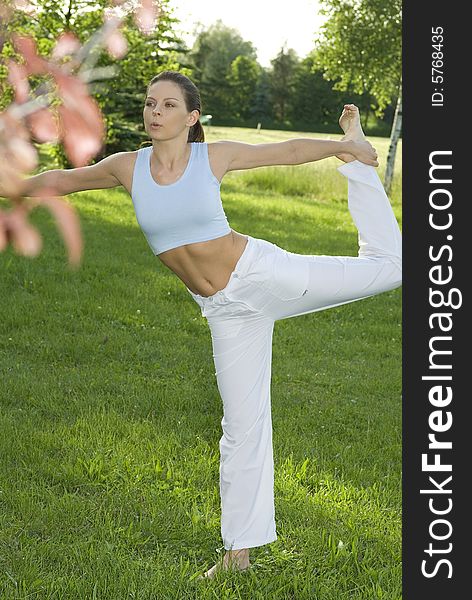 Sporty girl exercising on meadow against the sky.