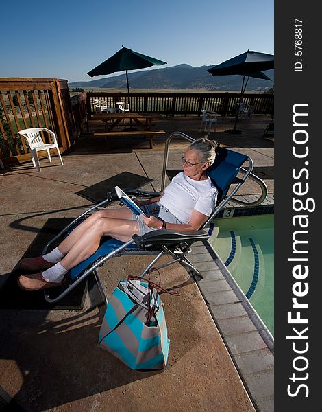 Senior woman sitting by pool reading book