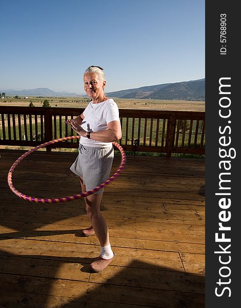 Senior woman hoola hooping on wooden deck with view