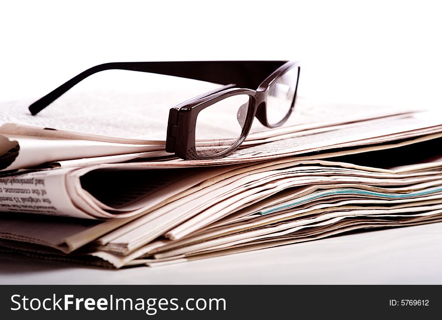 A pair of black reading glasses on top of a stack of newspapers on a white background. A pair of black reading glasses on top of a stack of newspapers on a white background