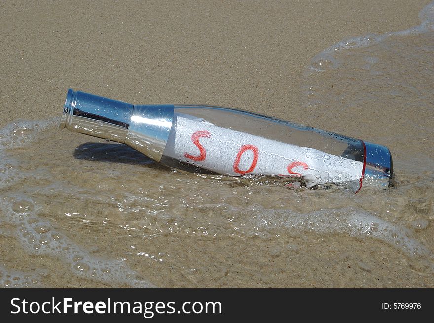 Message in a bottle with SOS signal lying in surf