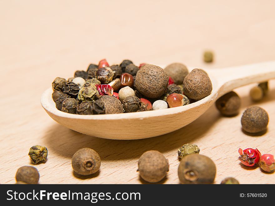 Wooden spoon filled with a mixture of grains of pepper are on a wooden surface