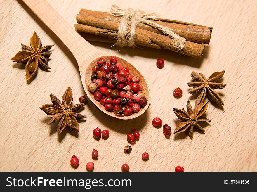 Wooden Spoon with a mixture of grains of pepper, cinnamon and star anise on a wooden surface