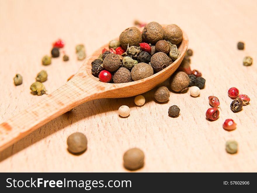 Wooden spoon filled with a mixture of grains of pepper are on a wooden surface