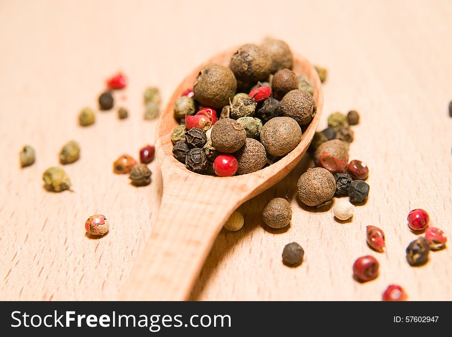 Spoon filled with a mixture of grains of pepper are on a wooden