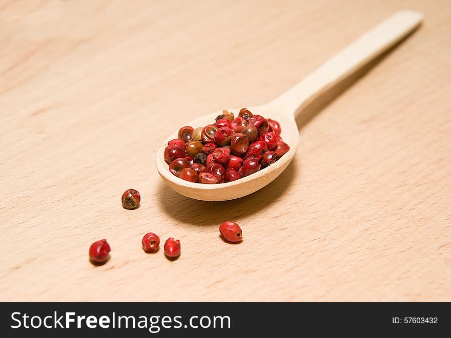 Wooden spoon filled with a mixture of grains of pepper are on a wooden surface