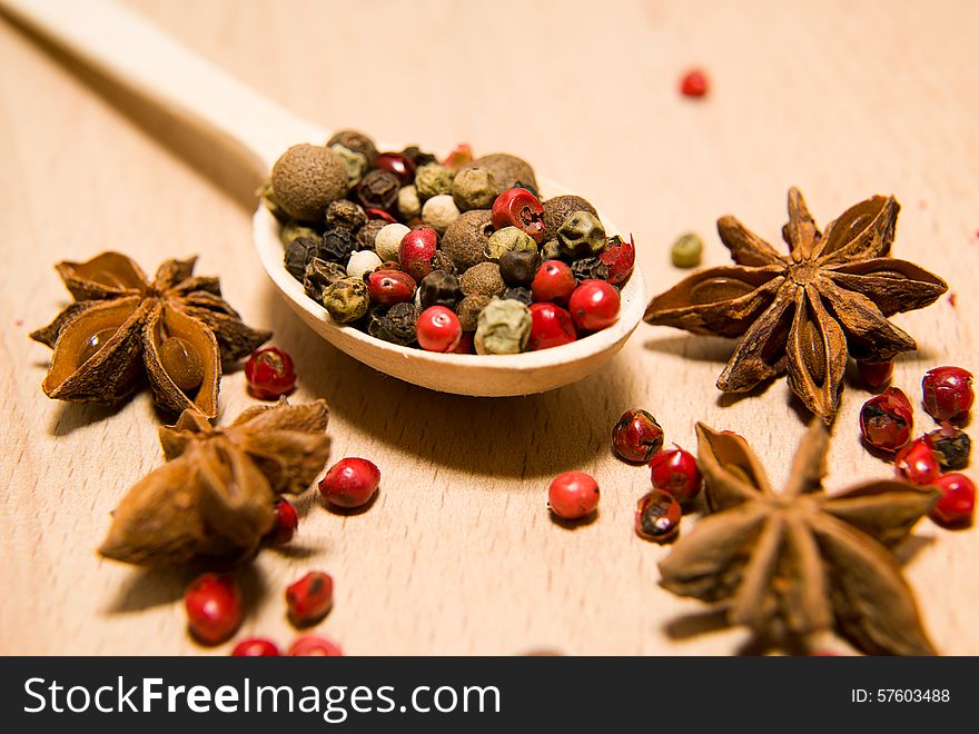 Wooden spoon filled with a mixture of grains of pepper and star anise on a wooden surface