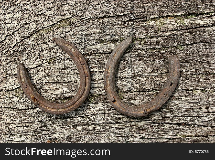 Two metal horseshoes on a piece of seasoned oak. Two metal horseshoes on a piece of seasoned oak.