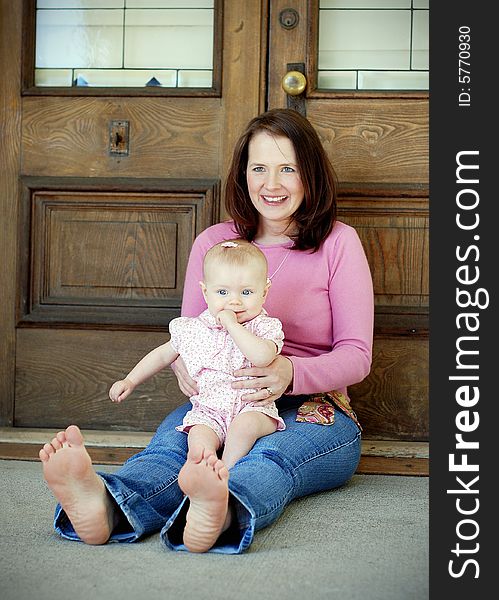 A mother, sitting down, learning against a wooden door, plays with her daughter, dressed in pink. Vertically framed shot. A mother, sitting down, learning against a wooden door, plays with her daughter, dressed in pink. Vertically framed shot