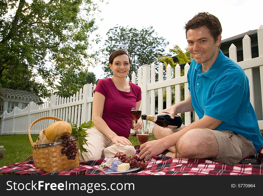 Couple with a picnic spread with wine, cheese and bread.  They are smiling and facing the camera. Horizontally framed shot. Couple with a picnic spread with wine, cheese and bread.  They are smiling and facing the camera. Horizontally framed shot.